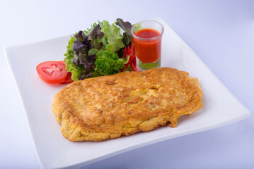 Golden minced pork omelet, chopped tomatoes, salad greens, and tomato sauce on a white plate, white background.