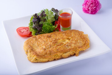 Golden minced pork omelet, chopped tomatoes, salad greens, and tomato sauce on a white plate, white background.