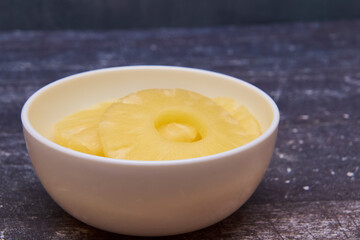 Sliced ​​pineapple, canned preserve. Close-up photograph with copy space on a table against a rustic background.