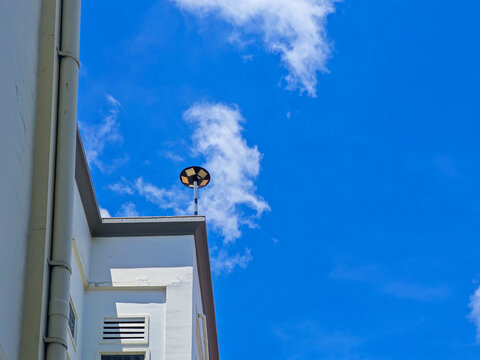 White building's facade meets a clear blue sky dotted with fluffy clouds.  A lamp post sits atop the building, blending nature and architectural elements together into a serene urban landscape.