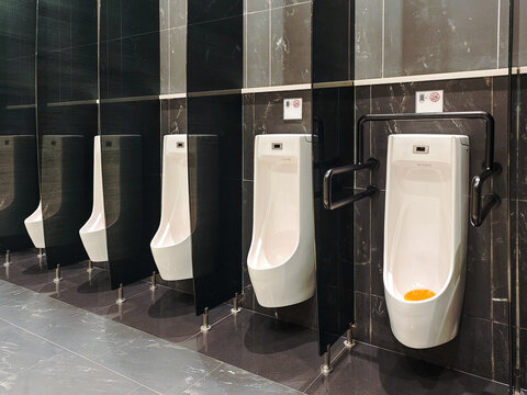 Row of modern, white urinals against a dark tile background, offering a sleek and sanitary look. The design highlights minimalist elegance and functional elements for restroom interiors.