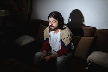 Fototapeta premium Man Watching TV in Dark Living Room with Dramatic TV Light