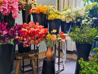 Colorful display of fresh flowers arranged in black buckets inside a florist shop. A variety of vibrant blooms pink tulips, roses, white flowers, greenery, and mixed seasonal plants in flower shop