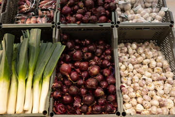 Fresh vegetables are presented in boxes in the shop window. They include leeks, red onions and garlic.