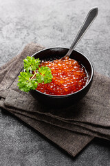 Red caviar in black bowl with parsley on dark table