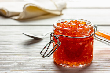 Red caviar jar with spoon on wooden background