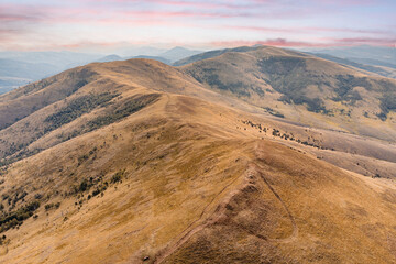 Aerial view capturing a wide mountainous landscape with a golden ridge leading toward a distant valley in Zlatibor, Serbia