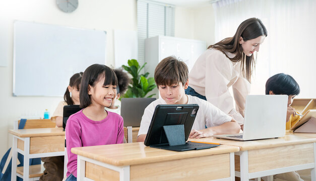 Portrait of smile teacher help elementary school children with digital tablets desks, show technology integration modern learning in classroom. Back to school, education.