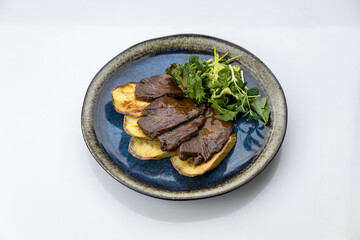 Sliced beef with gravy over roasted potatoes and greens on ceramic plate, overhead