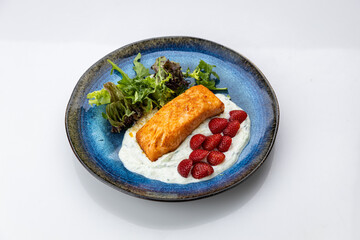 Seared salmon fillet with yogurt sauce, fresh strawberries and greens on blue ceramic plate