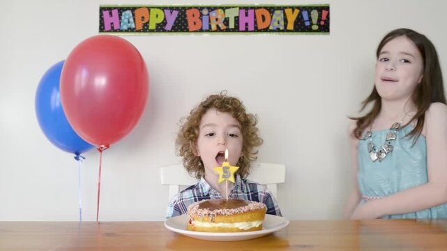 Sister singing Happy Birthday to her younger brother on his 5th birthday blowing out a candle on a cake; Australia