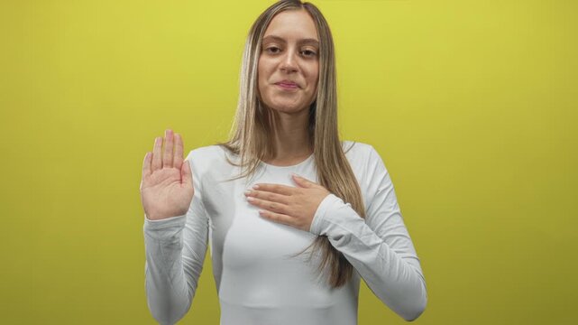 Young woman places hand on chest and raises other palm in a studio, long hair and white long sleeve top; sincerity pledge.