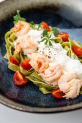 Gourmet spinach tagliatelle with shrimp, burrata and cherry tomatoes in ceramic bowl