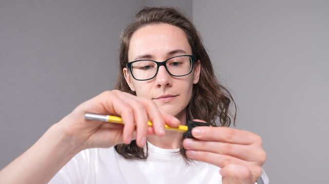 Young woman with glasses concentrating on delicate repair work, holding a small electronic device and a screwdriver, demonstrating focus on technology maintenance or diy project
