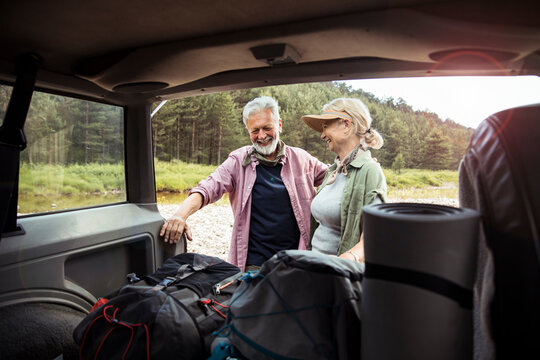Happy senior couple packing hiking gear at car in forest