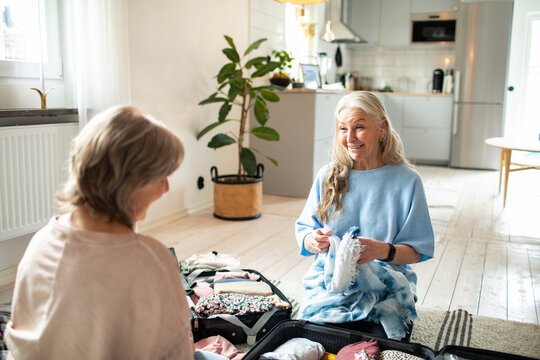 Senior lesbian couple smiling while packing luggage at home