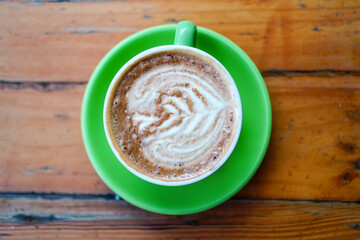 Elevated view of a creamy latte art with latte served in a bright green saucer with a simple wooden backdrop, perfect for illustrating morning routines and coffee breaks and warm beverage enjoyment.