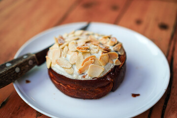 Close-up shows a delightful pastry with toasted almonds and cream filling on a white plate, a rustic knife rests nearby. Perfect for showcasing bakery delights and gourmet desserts in culinary themes.