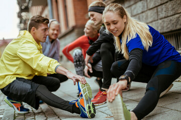 Young adults smiling while stretching before run on city street