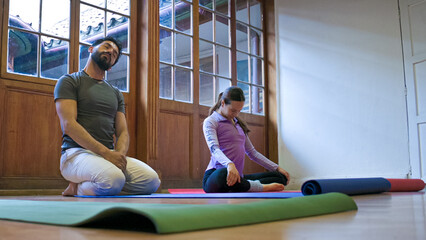 Obraz premium Two friends relaxing on yoga mats to begin yoga session in a studio with wooden doors and large windows.