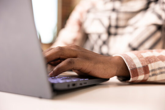 Close up on black man typing on laptop keyboard, updating online blog post. African american male individual seated at desk, using digital device to write business reports and gather financial data.