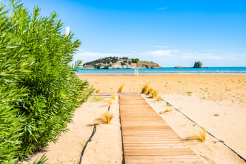 Wooden pathway leading through sand dunes toward the calm blue sea and Isola di Varano near Vieste, Apulia, Italy