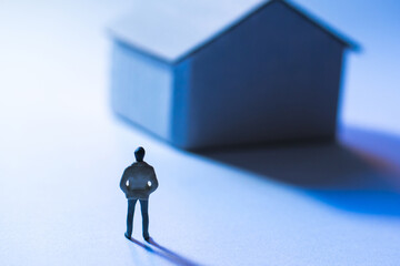 Miniature figure of person standing in front of a small house contemplating home and future possibilities