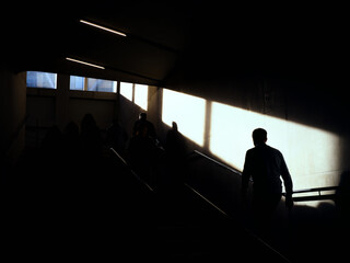 Silhouette of a person walking upstairs into the light. sunlight coming in directly from windows above the stairs. High contrast dark space