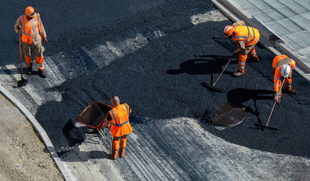 Des ouvriers du b&acirc;timent en tenue de s&eacute;curit&eacute; orange sont en train de goudronner une route avec de l'asphalte frais