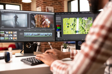 African american video editor working from home, using multiple screen setup to organize movie footage and timelines. Male post production artist making creative decisions in editing workflow.