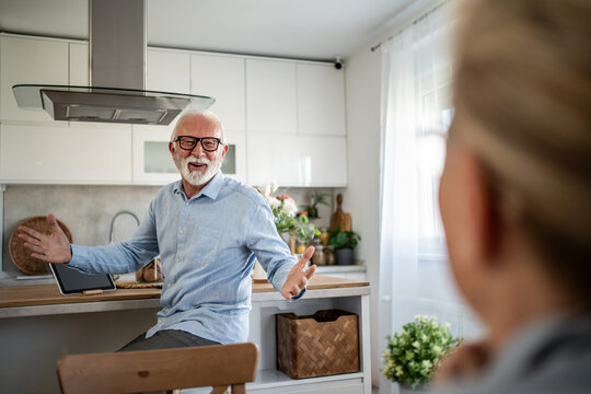 Senior man talking and gesturing to woman in kitchen - Powered by Adobe