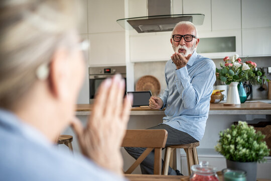 Senior man blowing kiss to woman in modern kitchen