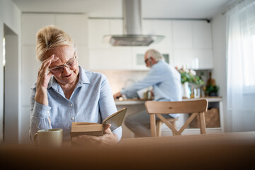 Senior woman having headache while reading book at home