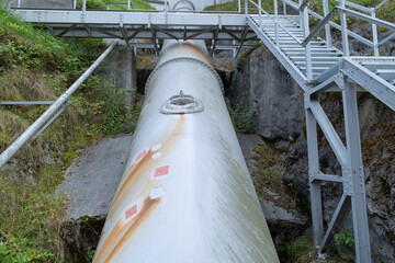 massive cylindrical metal water pipe extends vertically in a low-angle perspective,  orange rust streaks. The industrial vessel features visible seam rings and a circular access hatch