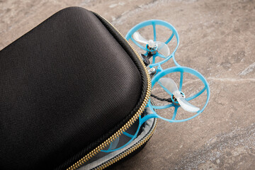 compact black zipper case partially holds a small FPV "Tiny Whoop" drone, with its two bright blue ducted propellers. quadcopter represents the beginner equipment for learning FPV flying.