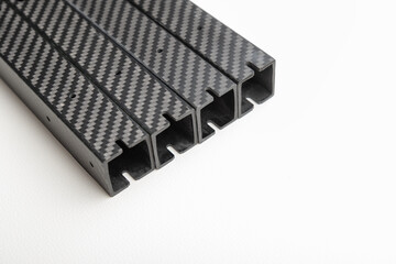 stack of four identical square-profile carbon fiber beams is diagonally placed on a clean white background.  lightweight composite parts arms for an FPV drone frame.