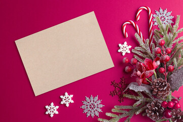 Christmas pink background with blank paper, poinsettia, decorative fir branch, candy canes and cones for tree decoraton. New Year winter holiday composition with decor and space for text, top view.