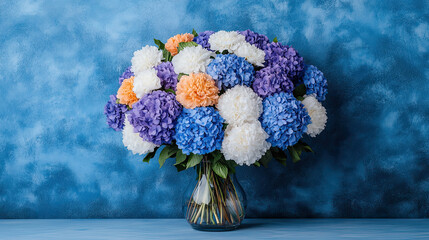 Colorful bouquet of hydrangea flowers in a glass vase with blue, purple, white, and orange tones, styled against a vibrant textured blue wall.