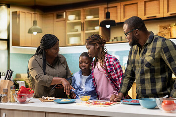 Fototapeta premium Parents teaching young kids how to make family recipe homemade pizza in the kitchen, explaining steps with ingredients to learn to cook efficiently. Making food in their cozy home.