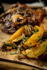Close-up of golden fried potato wedges with herbs, blurred roasted meat in back