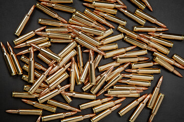 A large pile of golden brass rifle cartridges scattered across a dark back