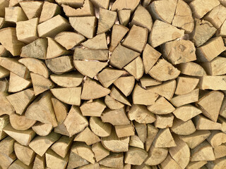 A close-up, full-frame texture of neatly stacked, split firewood. The seasoned logs form a dense, rustic background and geometric pattern perfect for themes of winter, warmth, and natural energy