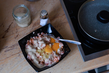 Bowl with minced meat, breadcrumbs and a raw egg on an authentic home kitchen counter. Concept of traditional cooking, homemade meal prep and food design.