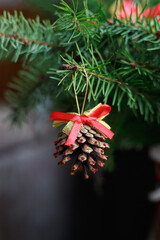 Pinecone with a red bow hanging on fir branches as handmade eco decor. Concept of natural DIY styling, Christmas mood and winter design.