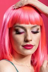 Stylish female model with defined facial features, posing with composed expression for camera. Face closeup of caucasian woman with bold makeup and pink wig against isolated background.