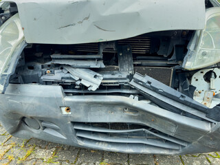 Damaged car front after an accident on a city street captured in the daylight showing broken pieces and a bent structure needing repair