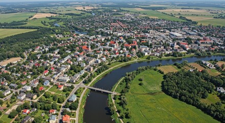 Aerial view of a town bisected by a river, with buildings, green spaces, farmland, and a bridge