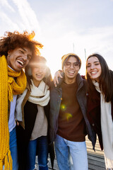 Four cheerful young multi-ethnic friends are hugging and laughing together during a sunny winter day