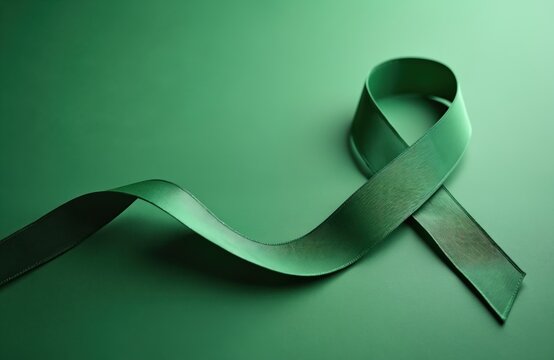 Green ribbon lies on green surface. Sign means symbolic support to lymphoma awareness or kidney cancer. Ribbon used for health awareness campaigns, charity and solidarity events. Copy space.