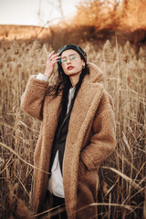 Elegant fashionable lady in brown fur coat over classic business suit on background of country autumn landscape
